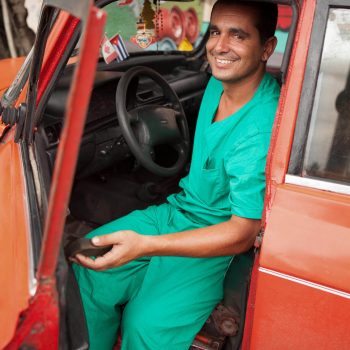 Portrait of man in green scrubs in orange car, Havana, Cuba