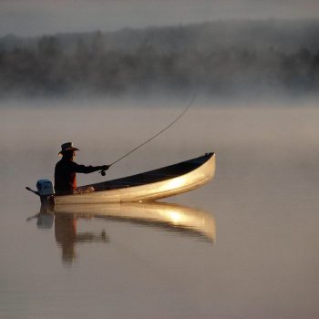 Fly fishing from canoe early morning calm lake with reflections Adirondacks, NY