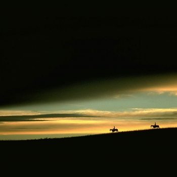 Horse riders silhouetted against dramatic sunset sky, Nebraska sand hills.