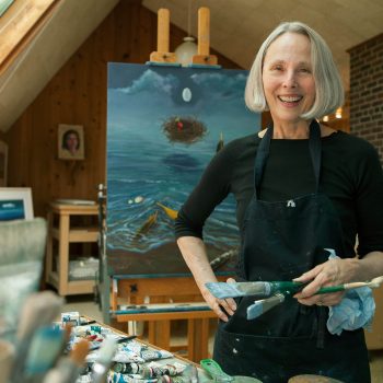 Mature woman artist in studio with paintings